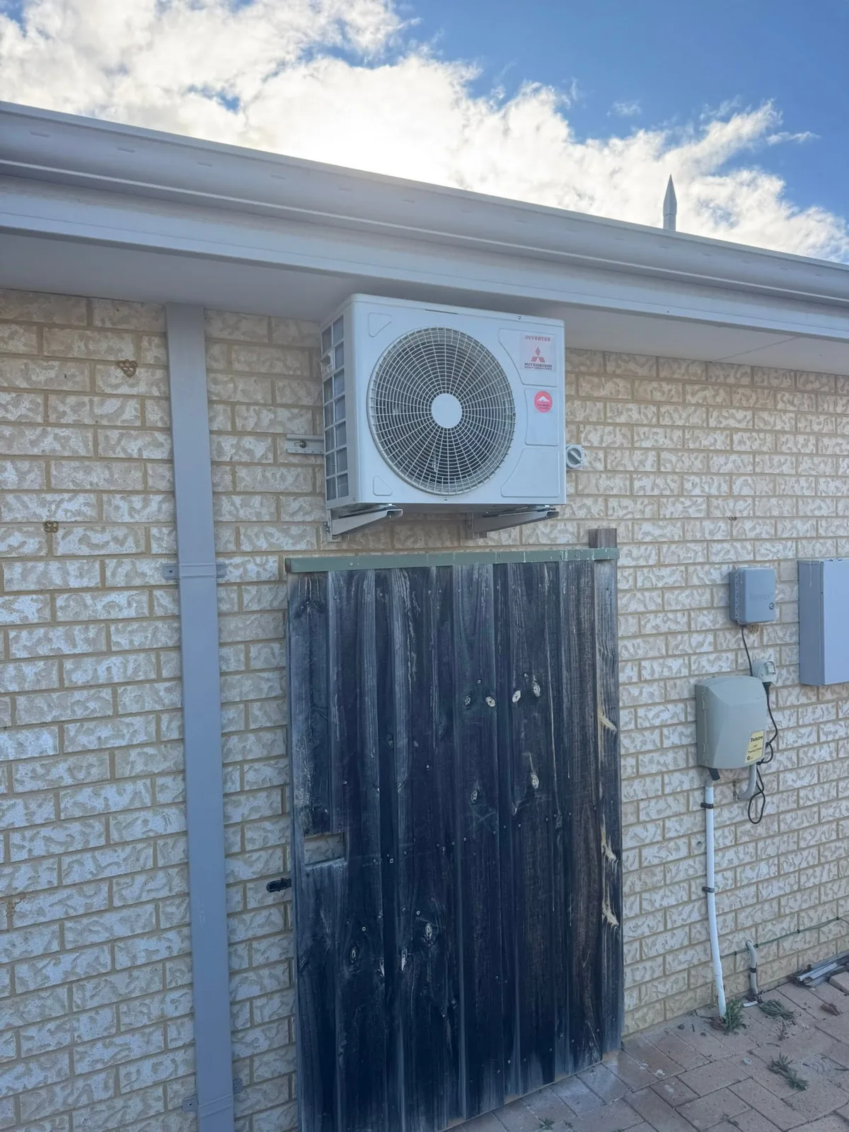 Mitsubishi Heavy Industries split system condenser bracket-mounted high on a brick wall under the eave