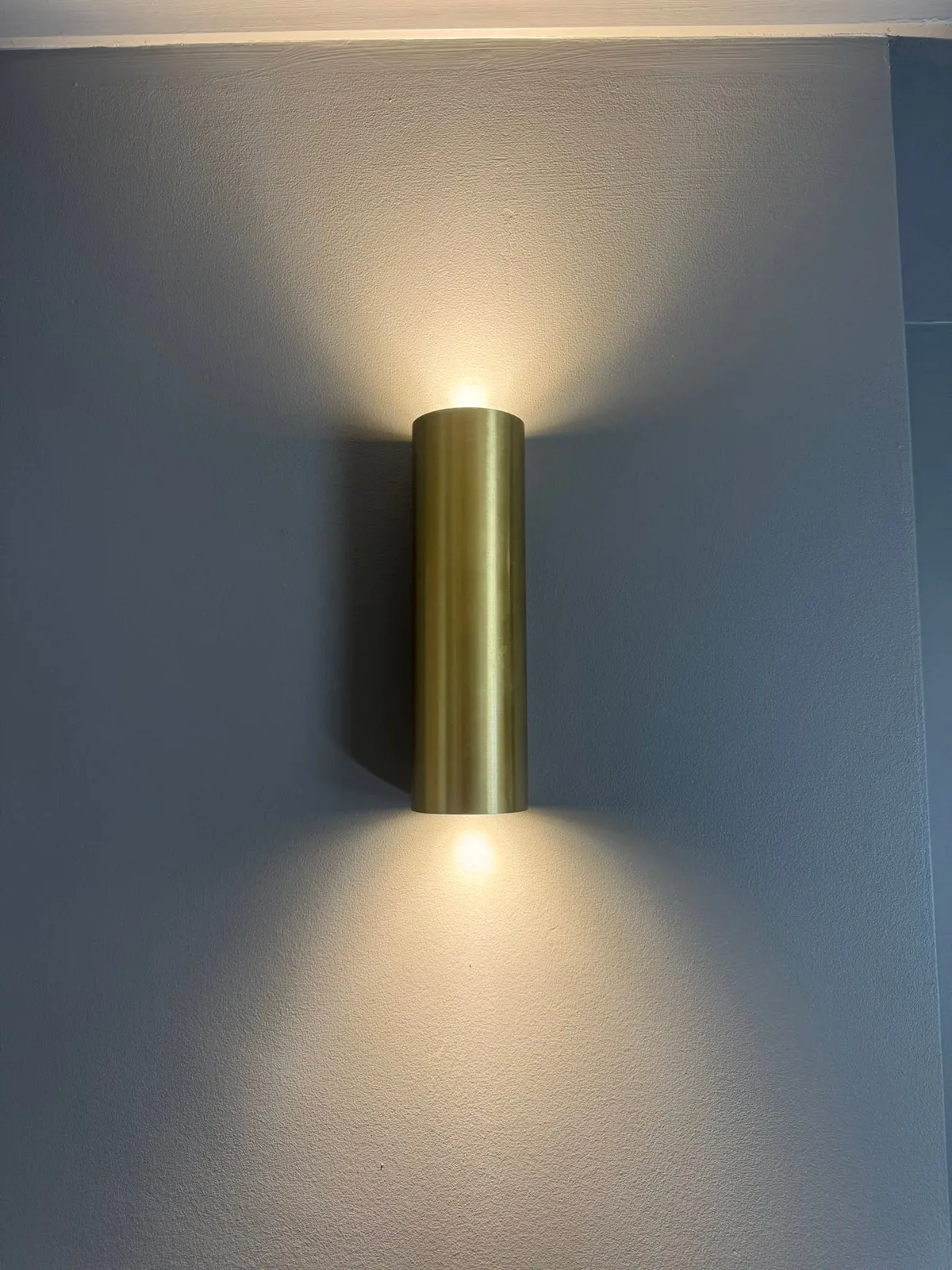 Close detail of a brass cylinder up-and-down wall light casting light on a painted wall