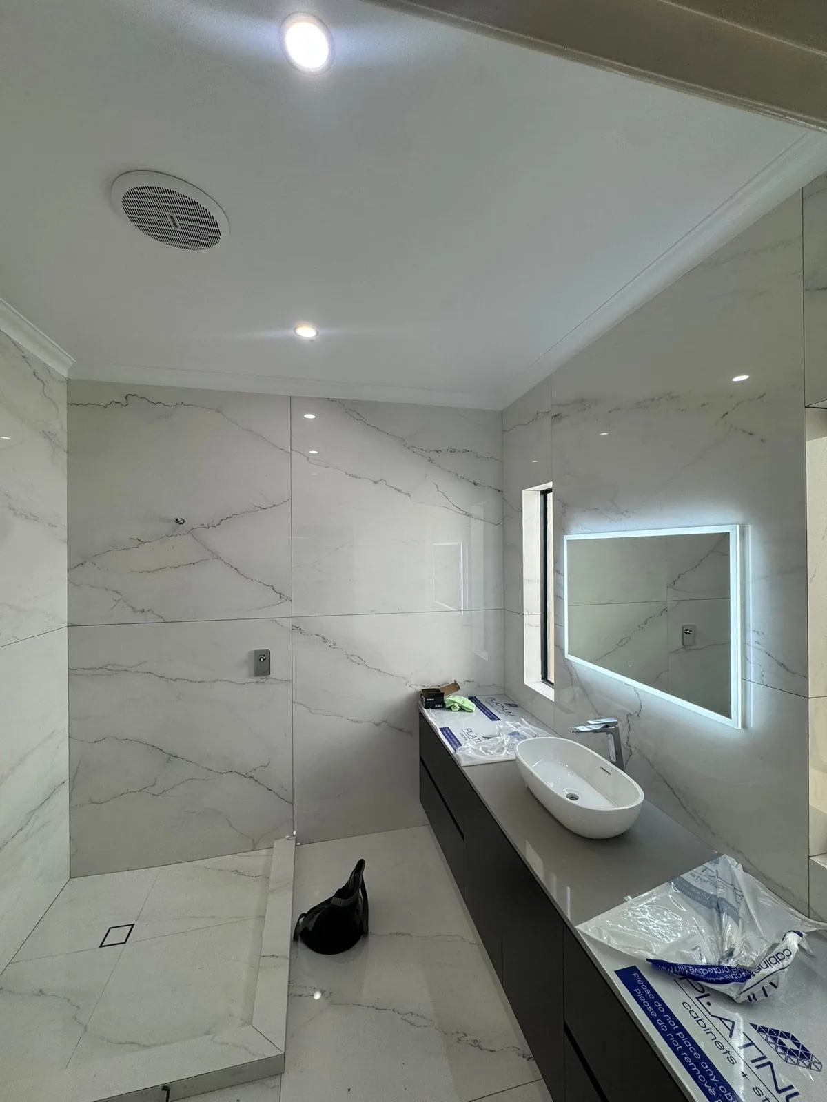 Marble-tiled ensuite with a vessel basin, backlit LED mirror, exhaust fan and downlights
