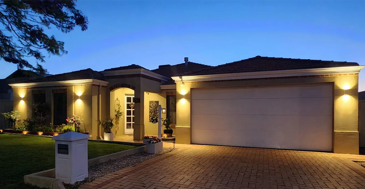 Full frontage of a residential home at dusk with garden, eave and entry lighting switched on