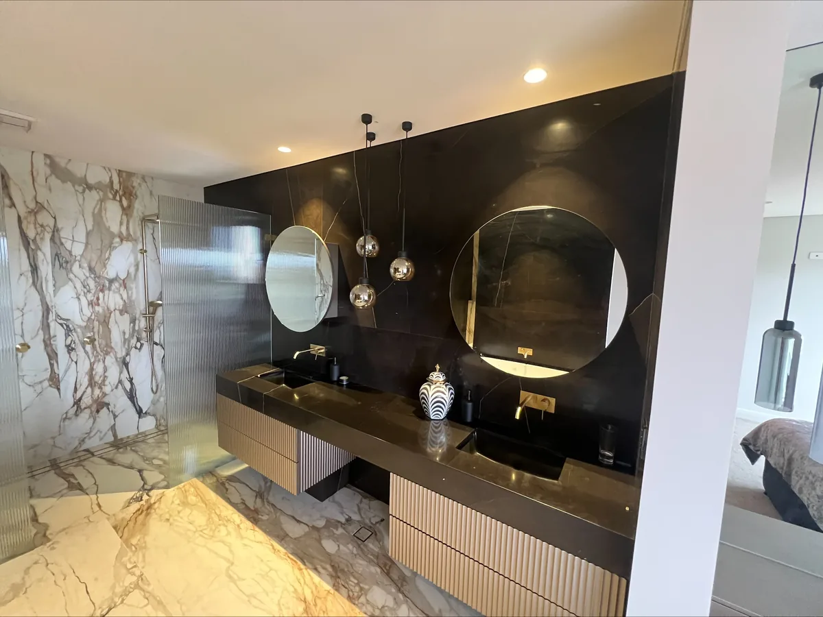 Luxury bathroom with full-height marble walls, round mirrors and hanging pendant lights