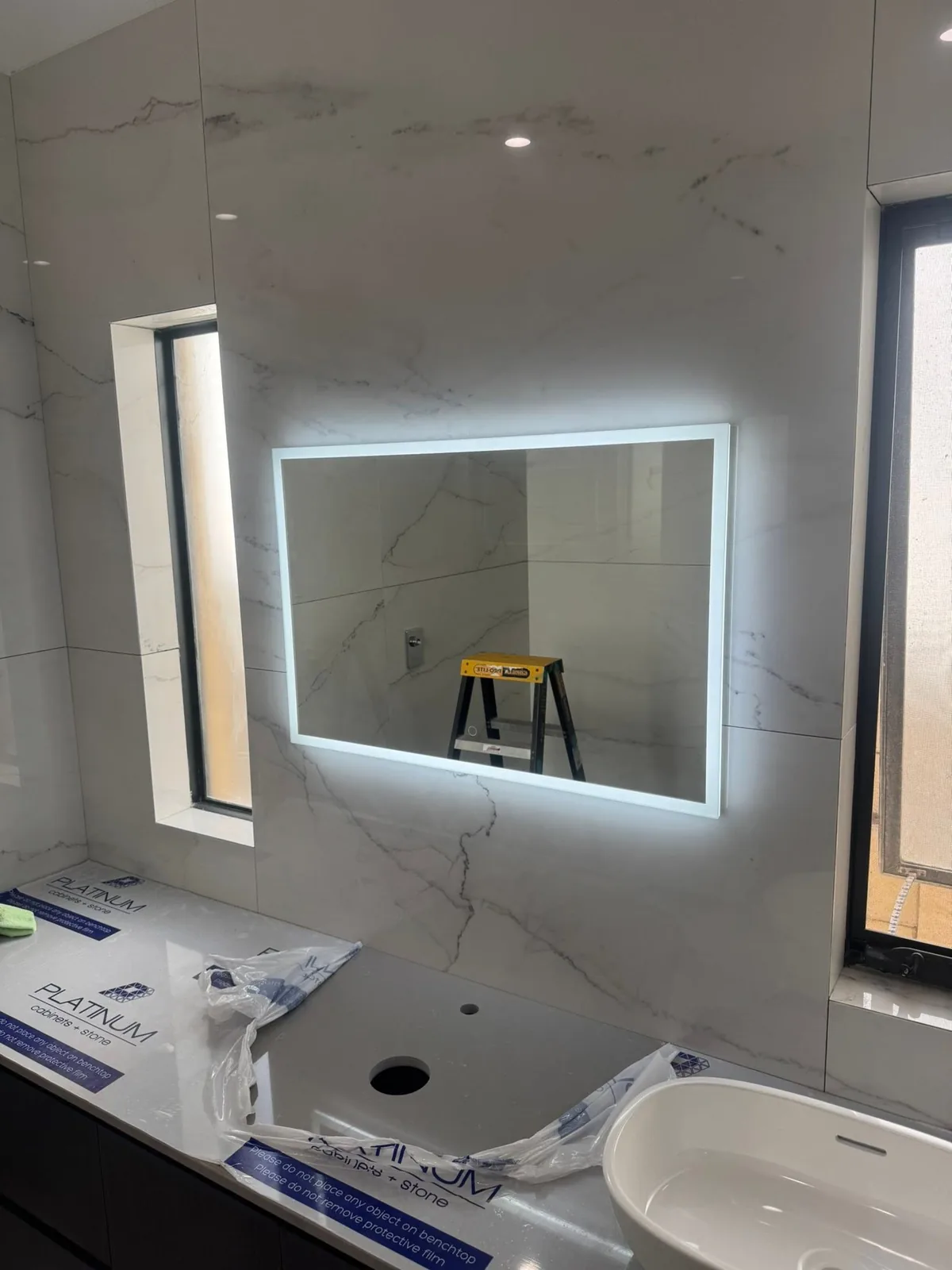 Backlit LED mirror above a basin and vanity in a full marble-tiled bathroom