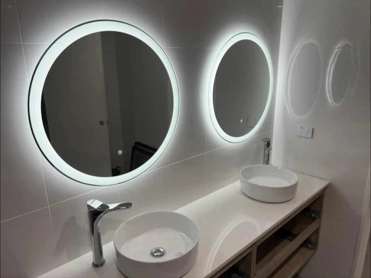 Two round backlit LED mirrors above twin vessel basins on a tiled vanity