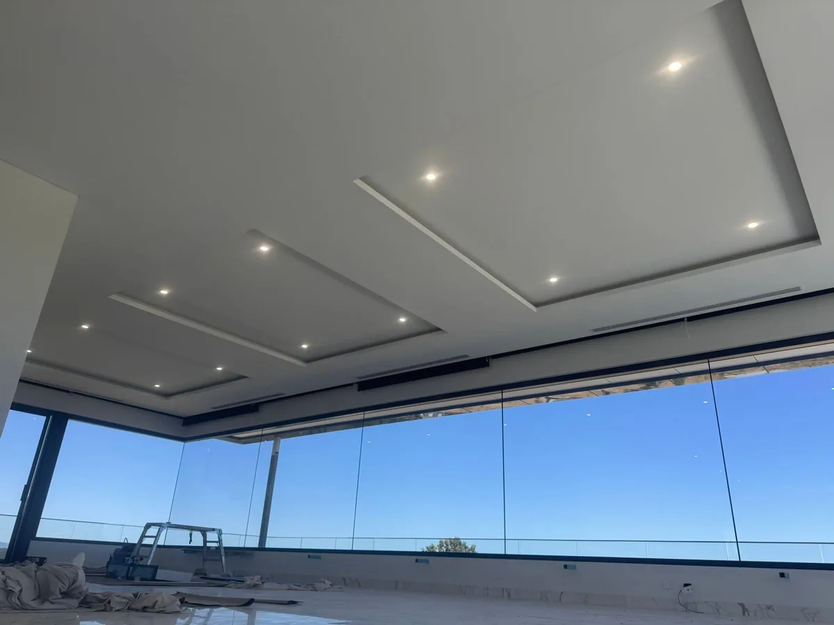 Stepped shadow-line ceiling with recessed downlights above panoramic full-height glazing in a new build