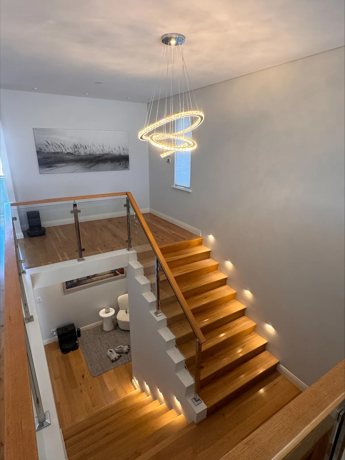 Timber staircase lit with LED step lights below a sculptural ring pendant in a double-height void