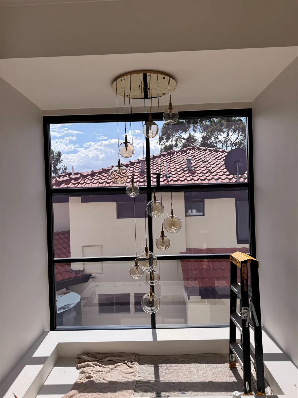 Cluster of glass pendant lights hung down a double-height void beside a black-framed picture window