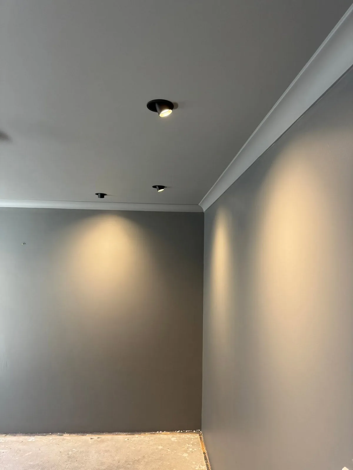Black adjustable gimbal downlights recessed into a ceiling and angled to wash light down a painted wall